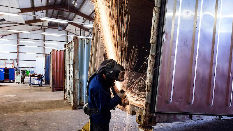 Blurry picture and bokeh of skilled worker wearing safety gloves uses an electric angle grinder to cut and smooth a metallic motorcycle exhaust component on a wooden workbench, creating bright sparks. Car Service.